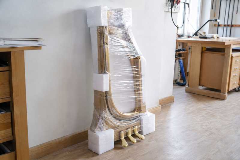Lyre de pedalier de piano emballee dans de la mousse de protection, posee contre un mur d'atelier