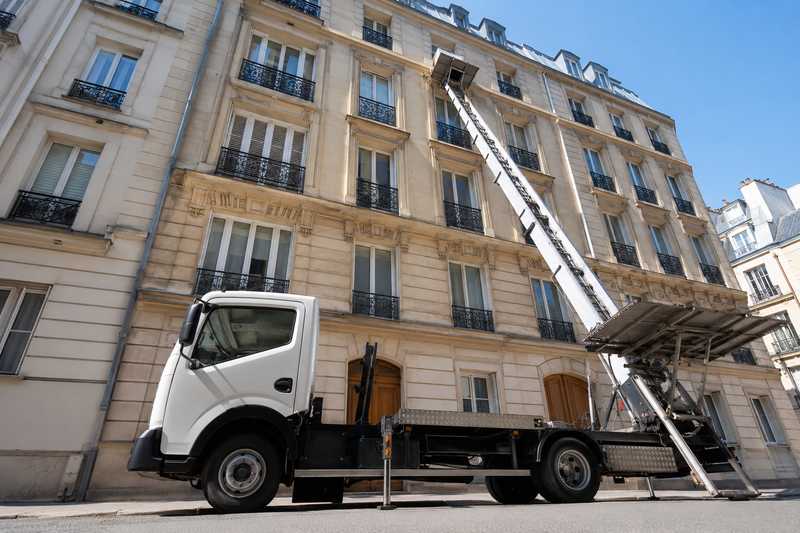Monte-meuble deploye contre une facade en pierre de taille, fleche pointee vers le quatrieme etage