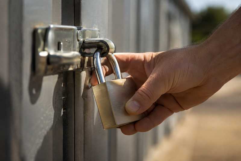 Main refermant un cadenas sur le loquet d'une porte de box de stockage en tole grise