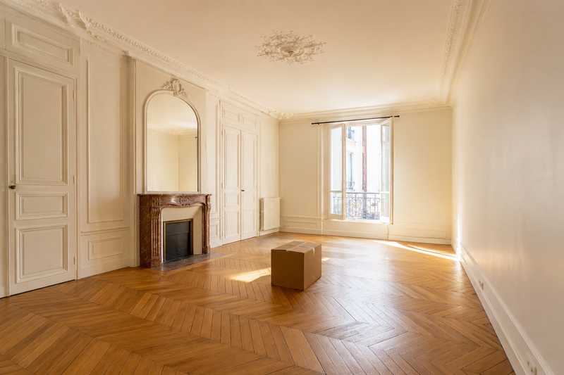 Studio parisien vide au parquet clair, un seul carton ferme au centre de la piece