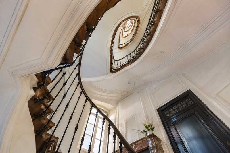 Cage d'escalier parisienne vue du rez-de-chaussee, volee etroite et rampe en fer forge